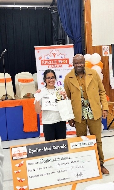 A young dark haired girl with glasses holding up an award next to an adult in a yellow suit.
